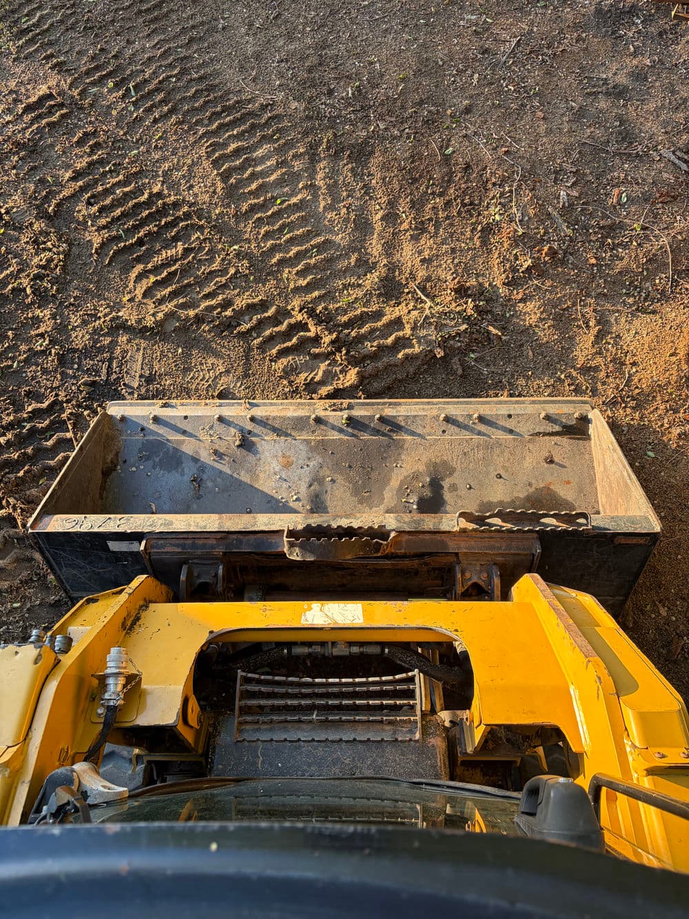 View from inside a yellow bulldozer with an attached blade on a dirt construction site.