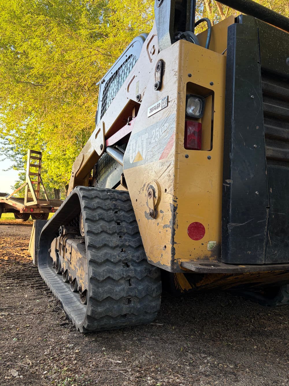 Caterpillar CAT 252B skid steer loader parked on gravel with trees in the background.